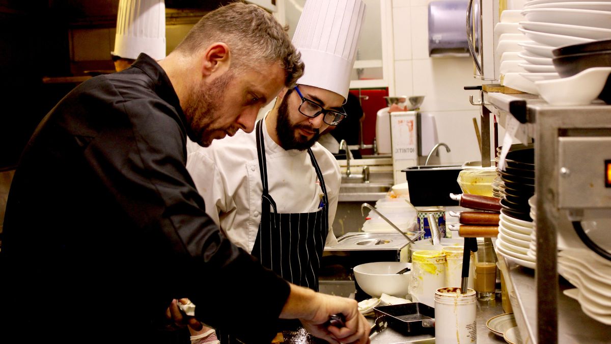 Chefs profissionais observando cuidadosamente o preparo de pratos na cozinha de restaurante, simbolizando a importância de evitar erros na cozinha.