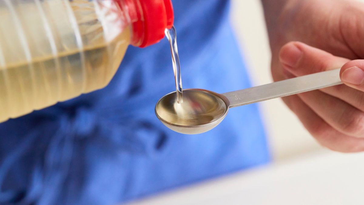 Uma pessoa despeja óleo de cozinha de uma garrafa em uma das colheres medidoras